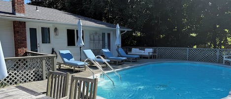 Una piscina con muelle de madera, sillones de descanso y chimenea de ladrillo.