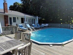 Ein Schwimmbecken mit Holzterrasse, Liegestühlen und einem Backsteinsschornstein.