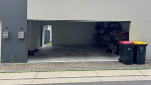 Ein Gebäudeeingang mit einer Garagentür, Briefkästen und Mülltonnen.
