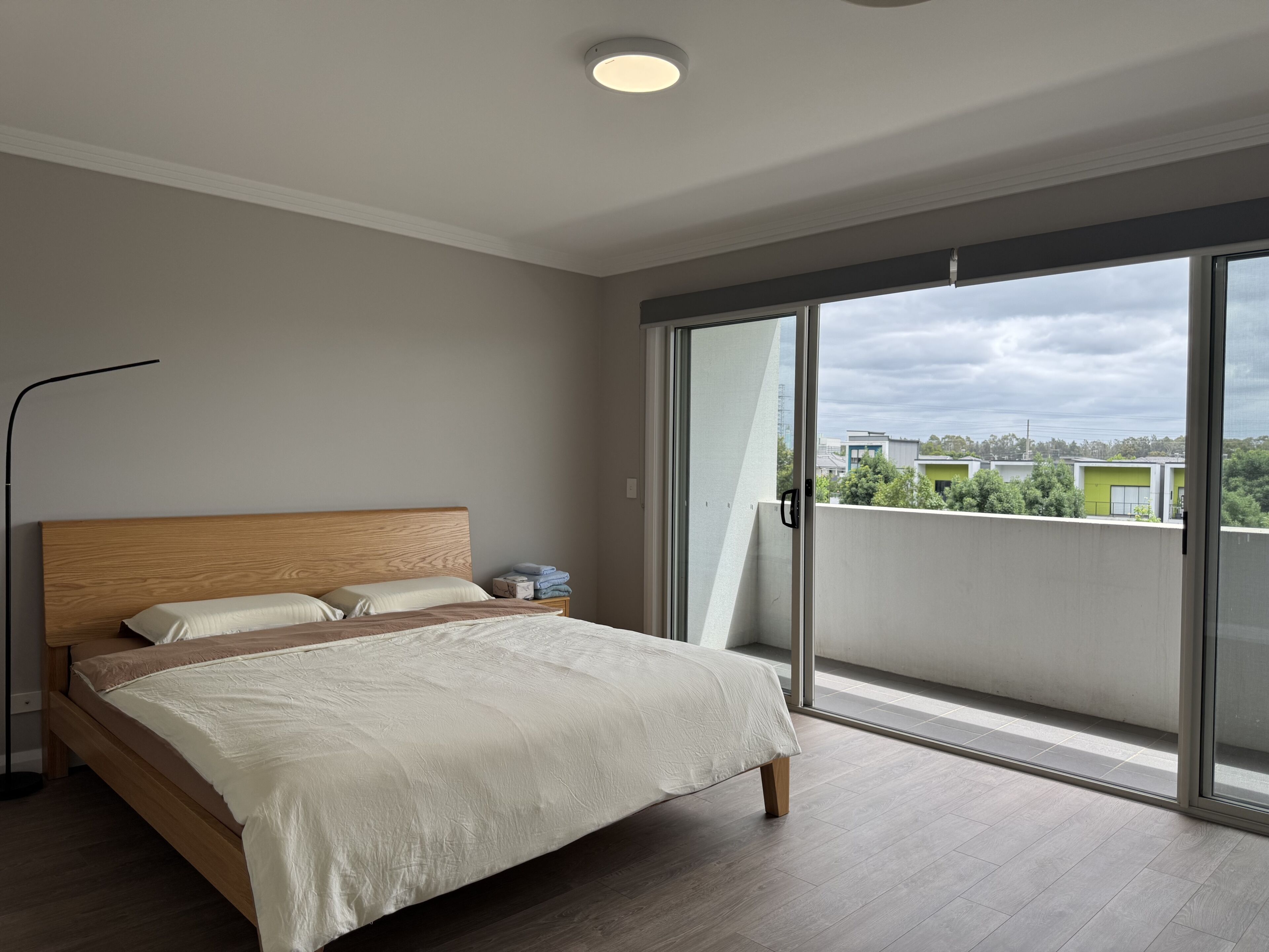 A bedroom with a large bed, a nightstand, a floor lamp, and a sliding glass door leading to a balcony.