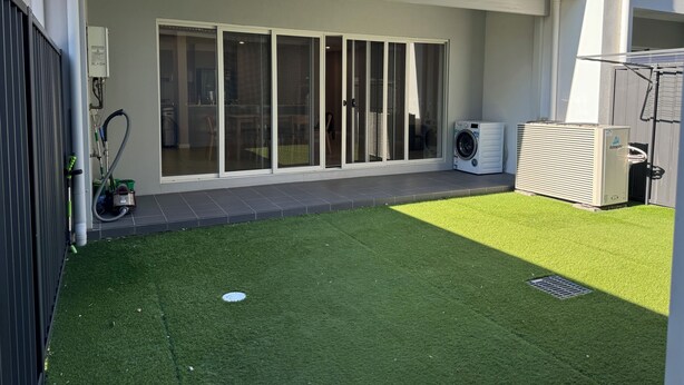 Ein Wohnhaus mit überdachter Terrasse, Waschmaschine und Rasenfläche.