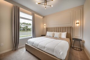 Une chambre à coucher avec un grand lit, une fenêtre avec des rideaux, un luminaire au plafond et une lampe fixée au mur.