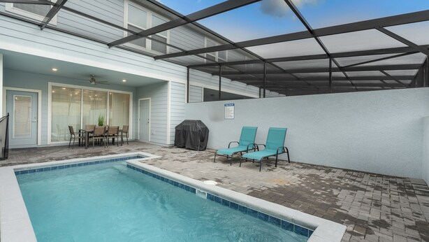 A swimming pool with a covered patio area, a table with chairs, and a grill. - Premium 5-Bedroom Resort Pool Home (Davenport)