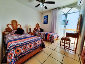 Ein Hotelzimmer mit zwei Betten, einem Deckenventilator, einem Tisch und Blick durch eine Glastür.