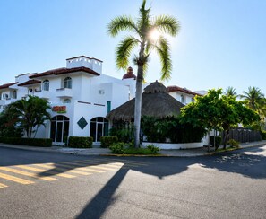 A white building with a thatched roof, palm trees, and a street view. - Dept. Exclusive Ixtapa (Ixtapa Zihuatanejo)