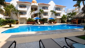 A hotel pool area with a clear blue pool, lounge chairs, palm trees, and a white building with balconies. - Dept. Exclusive Ixtapa (Ixtapa Zihuatanejo)