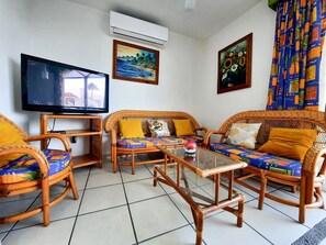 Ein Wohnzimmer mit Rattanmöbeln, einem Flachbildfernseher und Bildern an den Wänden.