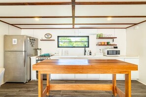 A modern kitchen with a large wooden table, stainless steel appliances, and a window with a view of greenery. - Secret Beach Escape with Pool! Off Season Rates! (San Pedro)
