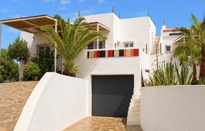 A modern building with a white facade, a dark garage door, and a staircase leading to a balcony.