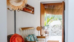 Ein Zimmer mit einem weißen Sofa, einem roten Hut, einem gewebten Wandbehang und Blick auf Grünfläche.