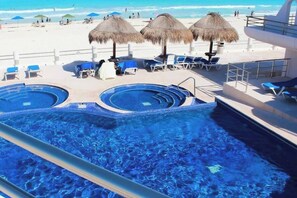 Ein Poolbereich mit mehreren Whirlpools und Liegestühlen mit Blick auf einen Strand.