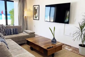 A living room with a sofa, a coffee table with wheels, a TV mounted on the wall, and a potted plant. - Top · Villa frente al mar · Playa a unos pasos (Cancún)