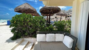 A balcony with a cushioned seating area, surrounded by thatched umbrellas, and overlooking a beach with a clear sky. - TOP/3BR/First Line Ocean Front Villa/2 Terrace/HZ (Cancún)