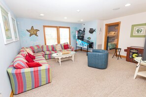A living room with a striped sofa, a coffee table, a blue ottoman, and a Star Wars-themed shelf. - Oceanside, 2 Hot Tubs- 2 Duplex's rents as 1-BU22, Love R Shack at the Beach (Corolla)