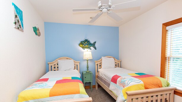A bedroom with two single beds, a ceiling fan, a wall-mounted lamp, and a window with blinds. - Oceanside, 2 Hot Tubs- 2 Duplex's rents as 1-BU22, Love R Shack at the Beach (Corolla)