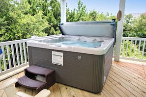 Ein Whirlpool auf einer Holzterrasse mit weißer Reling, umgeben von viel Grün.