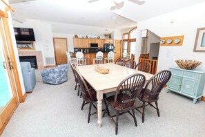 A dining area with a large table and chairs, a kitchen in the background, and a living room with a fireplace. - Oceanside, 2 Hot Tubs- 2 Duplex's rents as 1-BU22, Love R Shack at the Beach (Corolla)