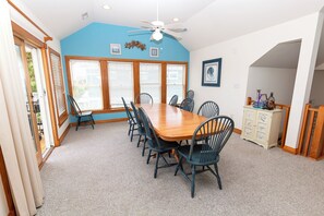 A dining room with a wooden table and chairs, large windows with blinds, a ceiling fan, and a cabinet with decorative items. - Oceanside, 2 Hot Tubs- 2 Duplex's rents as 1-BU22, Love R Shack at the Beach (Corolla)