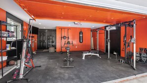 Un gimnasio con equipos de ejercicio variados, incluyendo una prensa de banca, una estructura para sentadillas y un saco de boxeo.
