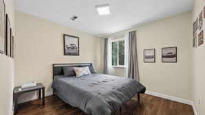 Un dormitorio con cama, mesita de noche, ventana con cortinas e imágenes colgadas en la pared.