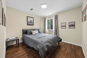 Un dormitorio con cama, mesita de noche, ventana con cortinas e imágenes colgadas en la pared.