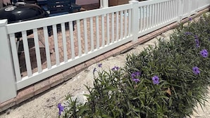 Een roze huis met een overdekte veranda, tuinmeubilair en een barbecue.