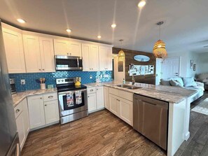 A modern kitchen with white cabinets, a built-in oven, a microwave, and a large island with a sink. - St. Pete Coastal Retreat with beautiful water view (St. Petersburg)