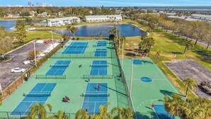 Een tenniscomplex met meerdere banen, een parkeerplaats en een waterpartij op de achtergrond.