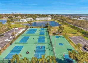 A tennis court complex with multiple courts, a parking area, and a body of water in the background. - St. Pete Coastal Retreat with beautiful water view (St. Petersburg)