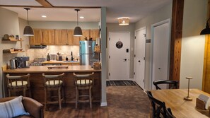 A modern kitchen with a central island, bar stools, wooden cabinets, and a stainless steel refrigerator. - Newly Renovated Slopeside Condo at Bryce Resort. Family and pet-friendly! (Mount Jackson)