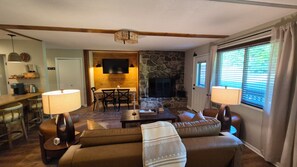 A living room with a stone fireplace, a television mounted on the wall, and a dining area with a table and chairs. - Newly Renovated Slopeside Condo at Bryce Resort. Family and pet-friendly! (Mount Jackson)