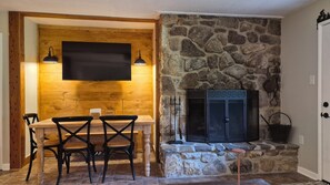 A cozy room with a stone fireplace, a wooden dining table with chairs, and a flat-screen TV mounted on a wooden wall. - Newly Renovated Slopeside Condo at Bryce Resort. Family and pet-friendly! (Mount Jackson)