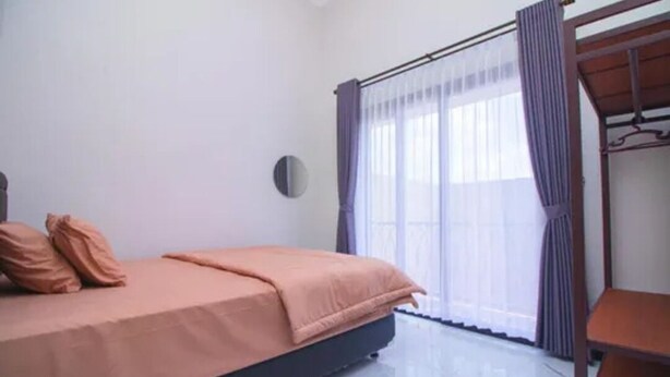 Une chambre à coucher avec un lit, une table de chevet, une fenêtre avec des rideaux et une horloge ronde fixée au mur.