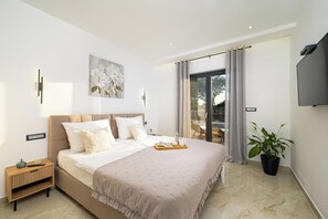 Une chambre moderne avec un grand lit, des tables de chevet, un tableau, une plante en pot et un téléviseur.