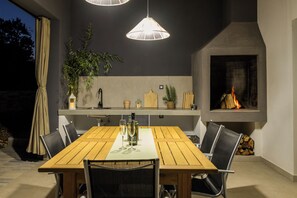 An outdoor dining area with a wooden table, chairs, hanging pendant lights, and a fireplace. - Villa Lenko (Istria - Svetvinčenat) (Svetvinčenat)