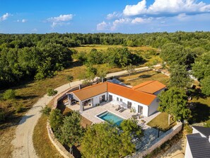 Une maison moderne avec une piscine, entourée d’un paysage boisé.