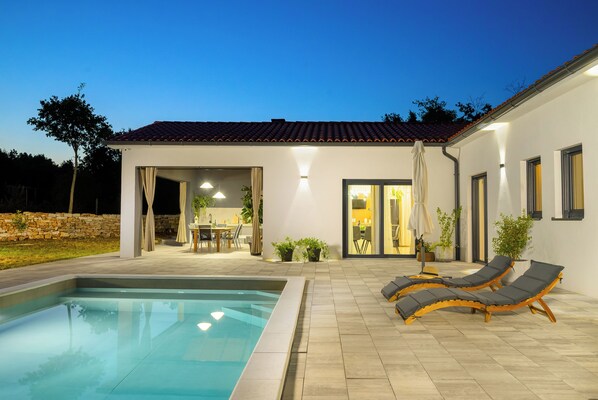 Une maison moderne dotée d’une piscine, d’un espace salon extérieur et d’un patio bien éclairé.
