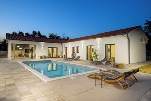 Ein modernes Haus mit Swimmingpool, Außenmöbeln und einer gut beleuchteten Terrasse.