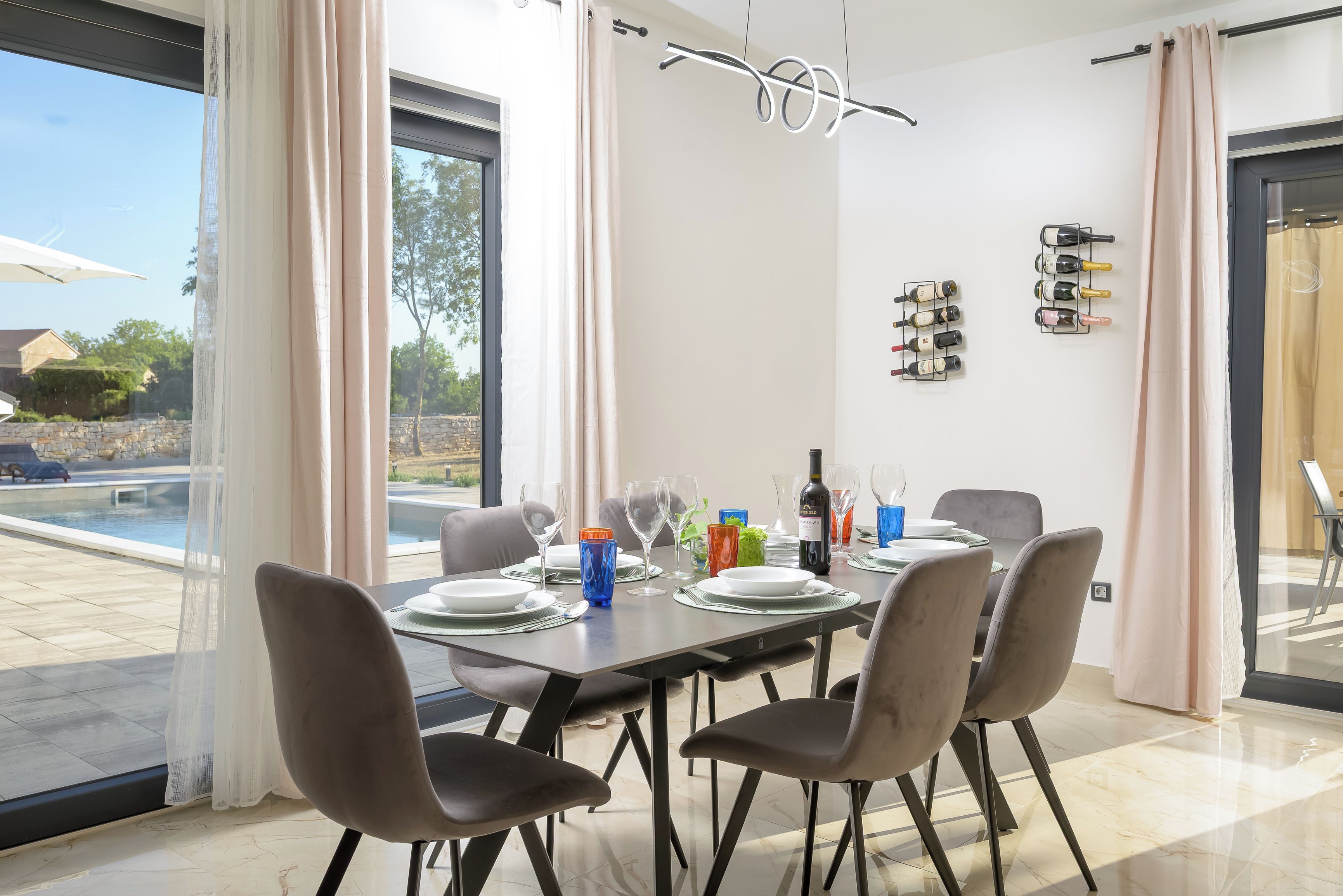 Un comedor con una mesa preparada para cuatro personas, sillas, una bodega de vinos y vistas a una piscina exterior.