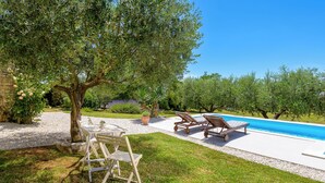 Zona de piscina con un árbol, dos sillones de descanso y una mesa.