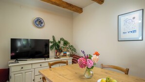 Un comedor con una mesa de madera, sillas, un televisor sobre un mueble, un florero con flores y un cuadro en la pared.