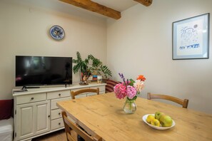 Ein Essbereich mit Holztisch, Stühlen, einem Fernseher auf einem Schrank, einer Vase mit Blumen und einem gerahmten Bild an der Wand.