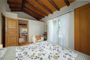 A bedroom with a wooden ceiling, a bed with a floral bedspread, a chair, and a window with curtains. - Villa Franciska (Istria - Svetvinčenat) (Svetvinčenat)
