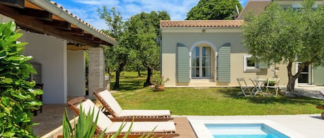 A poolside area with lounge chairs, a swimming pool, and a garden with trees and a lawn.