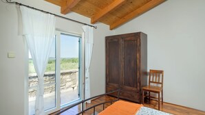 Un dormitorio con techo de madera, un armario, una silla y una cama con manta naranja.
