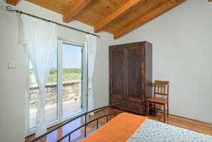 Ein Schlafzimmer mit Holzbalkendecke, einem Kleiderschrank, einem Sessel und einem Bett mit orangefarbener Decke.