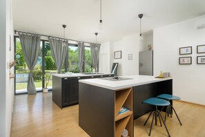 Une cuisine moderne dotée d’un îlot central, de tabourets de bar et offrant une vue sur la verdure environnante.