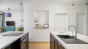 Una cocina moderna con encimeras blancas, horno empotrado, pileta con bol de vidrio e iluminación colgante.