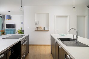 Eine moderne Küche mit weißen Arbeitsplatten, einem eingebauten Backofen, einer Spüle mit Glasbecken und Pendelleuchten.