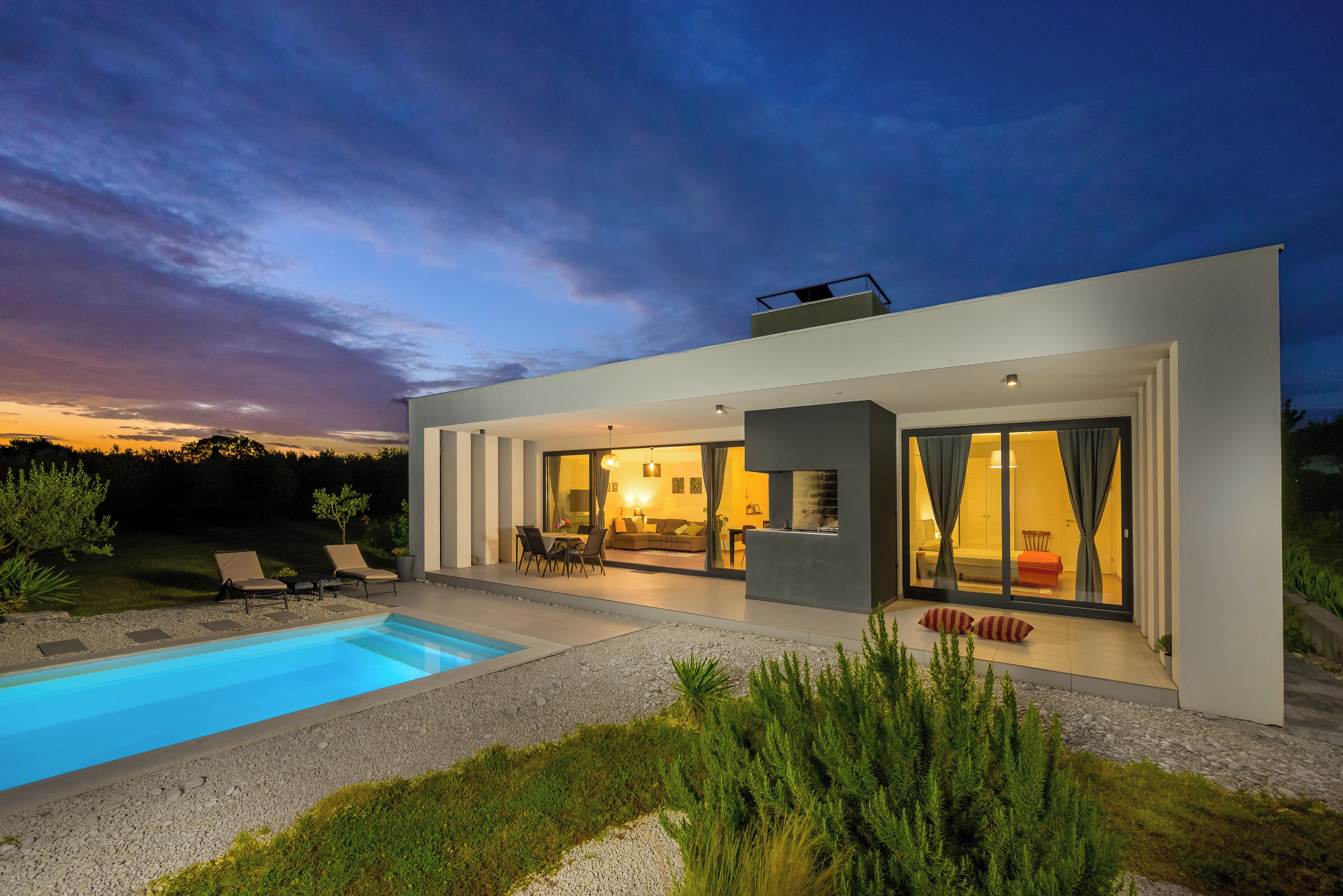 A modern house with a swimming pool, outdoor seating, and a large glass door leading to the interior.